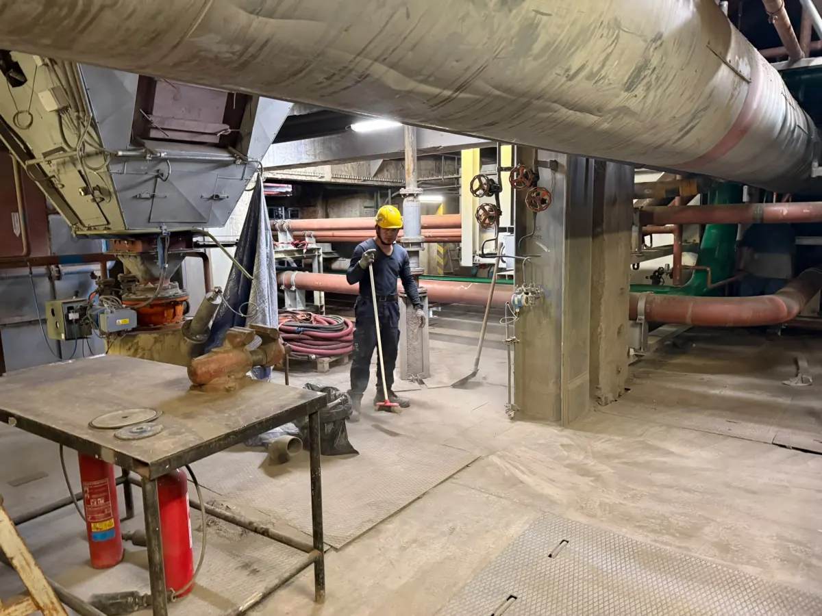 Pracovník v přilbě v průmyslové hale s potrubím a pracovním stolem