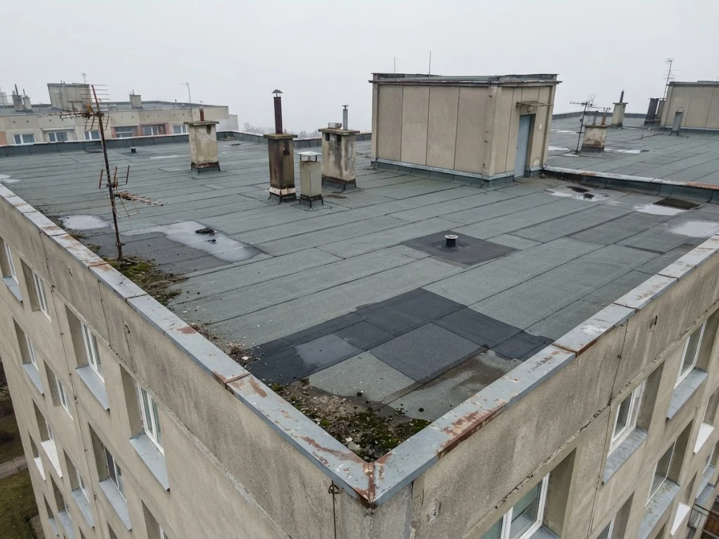 Plochá střecha panelového bytového domu s vpustí, atikou a výlezy z dronu