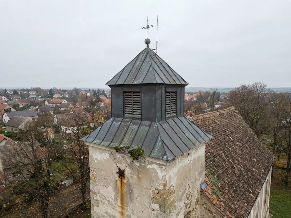 Věž vesnického kostela s plechovou střechou nasnímaná dronem z výšky